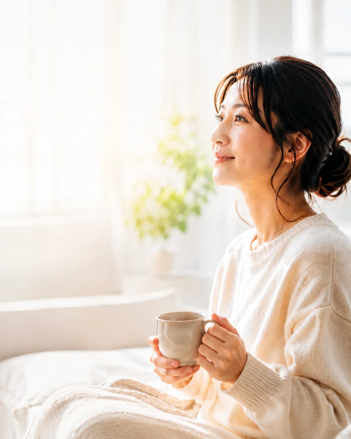 窓辺でマグカップを持ち、穏やかな表情を浮かべる女性